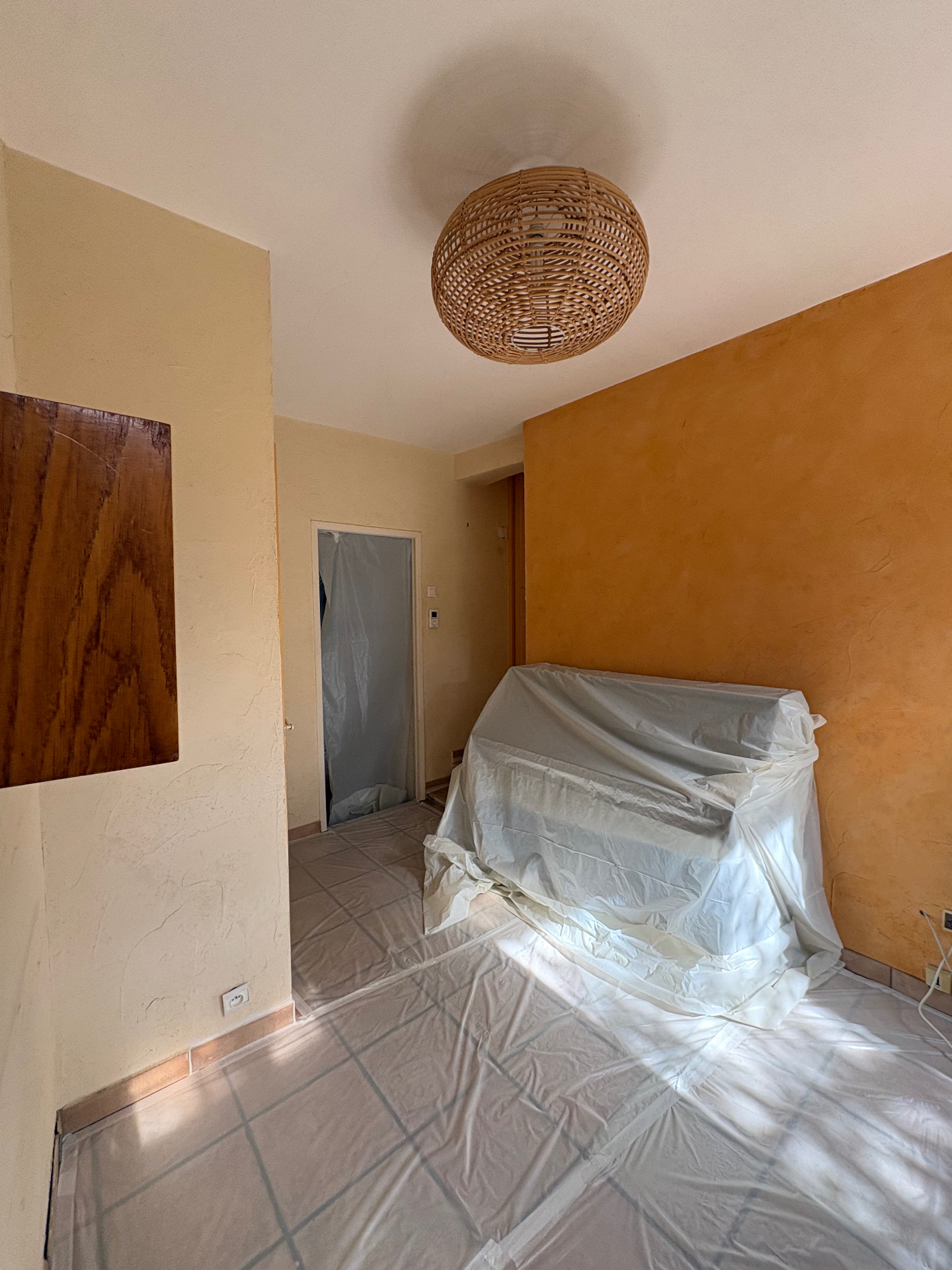 Pièce en cours de chantier, murs beiges et mur ocre, mobilier et sol protégés par des bâches