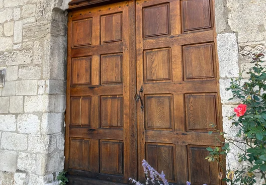 Porte ancienne en bois à caissons rénovée et lasurée dans un encadrement en pierre