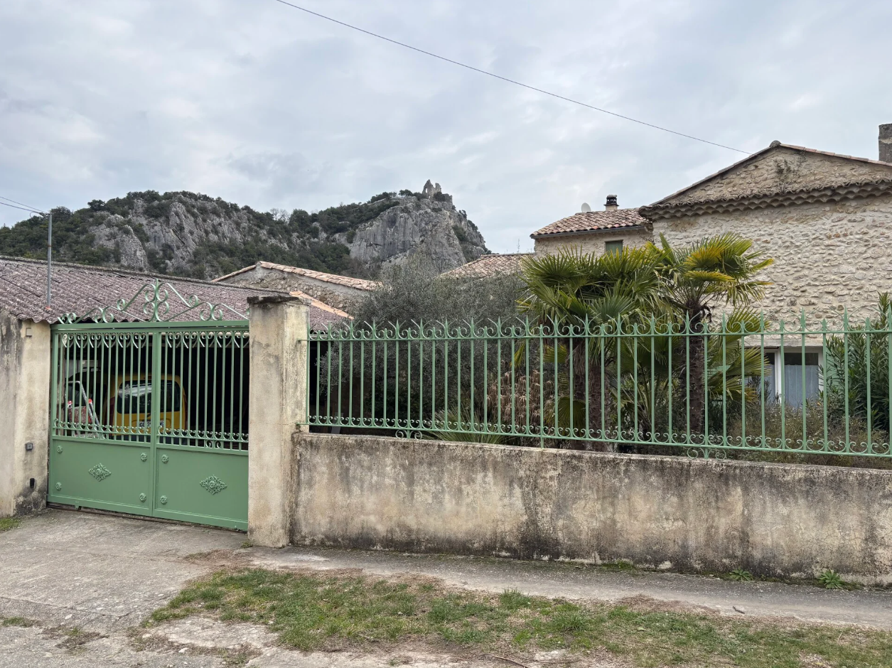 Portail en fer forgé repeint en vert d'eau et mur de clôture devant une maison ardéchoise